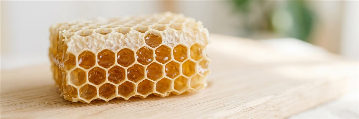 Fragmento de panal de abeja con miel sobre una tabla de madera clara