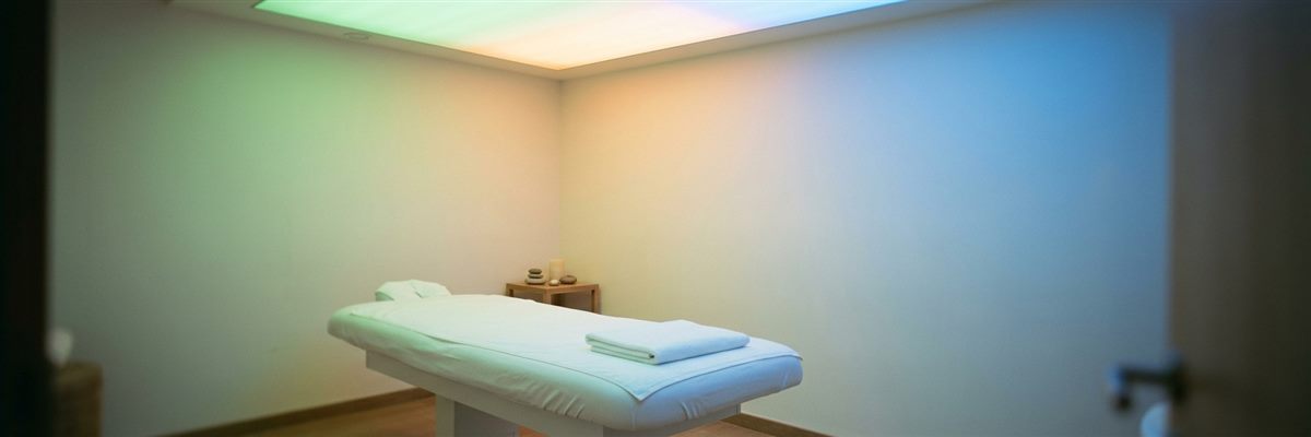 Sala de terapia iluminada con luz de colores suaves sobre la camilla